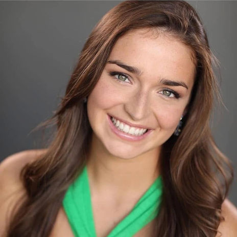 Smiling young woman with long brown hair and radiant green eyes.