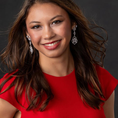 Young woman with long brown hair smiling, wearing red dress, earrings.