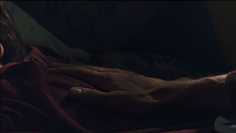 An older male hand gently rests on the boys back while he's fast asleep