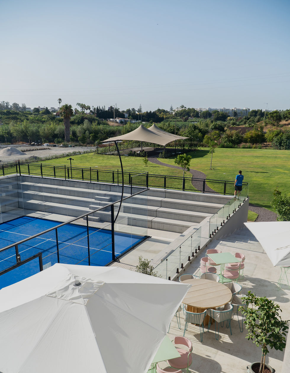 Aerial view of the blue outdoor padel courts at Unicorn Racket Club in Estepona, showing the main club building and parking area.