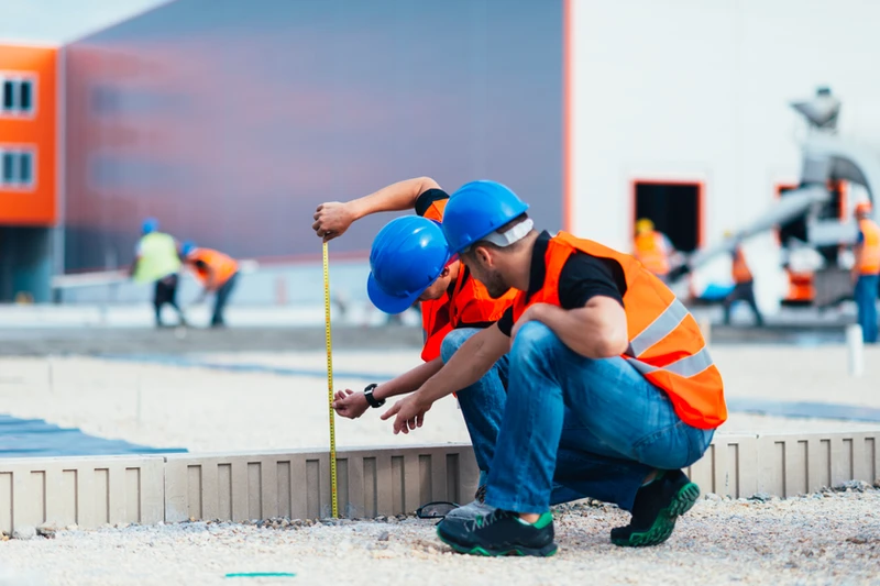 two construction workers are measuring something with a tape measure