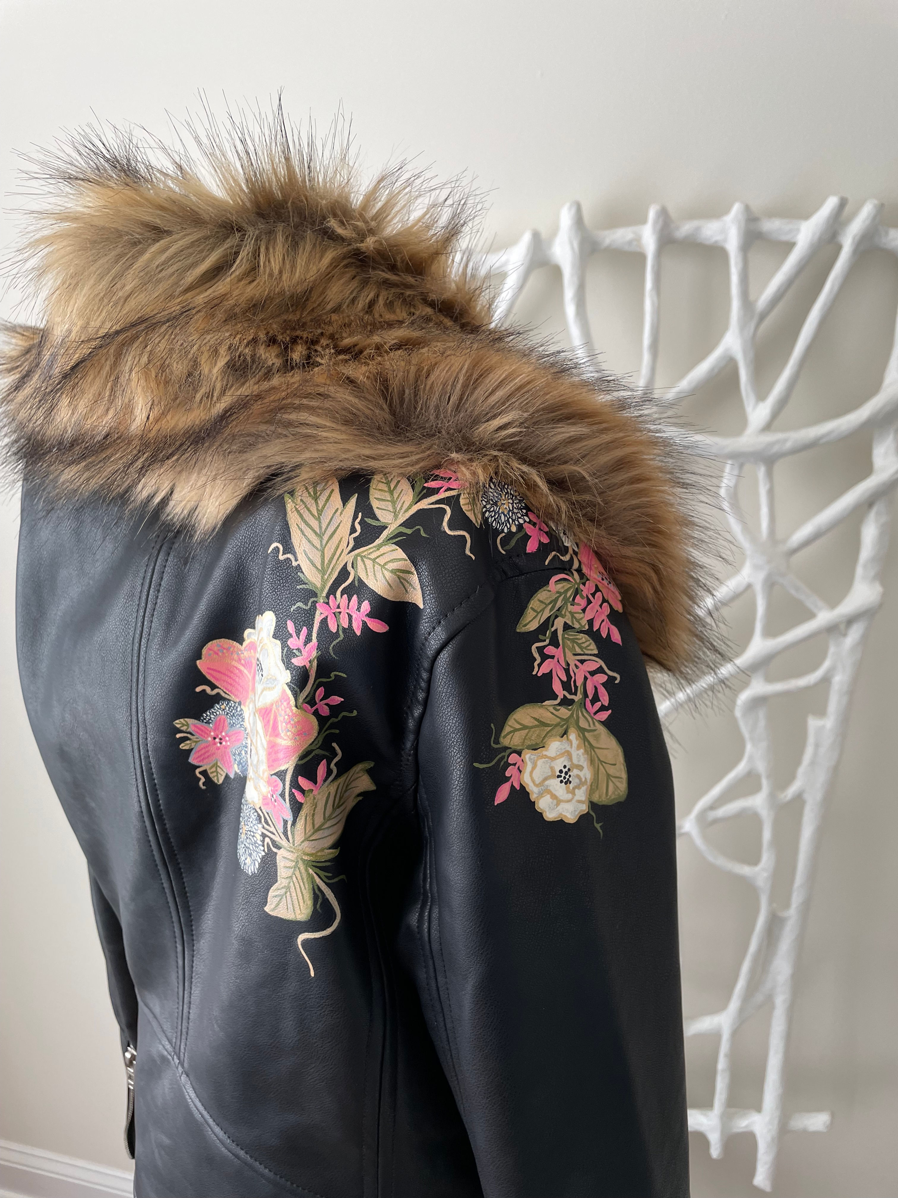 Black jacket with fur collar, floral embroidery, and decorative white backdrop.