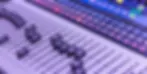 Audio mixing console with sliders and colorful illuminated buttons. Purple lighting creates a technical, vibrant mood.