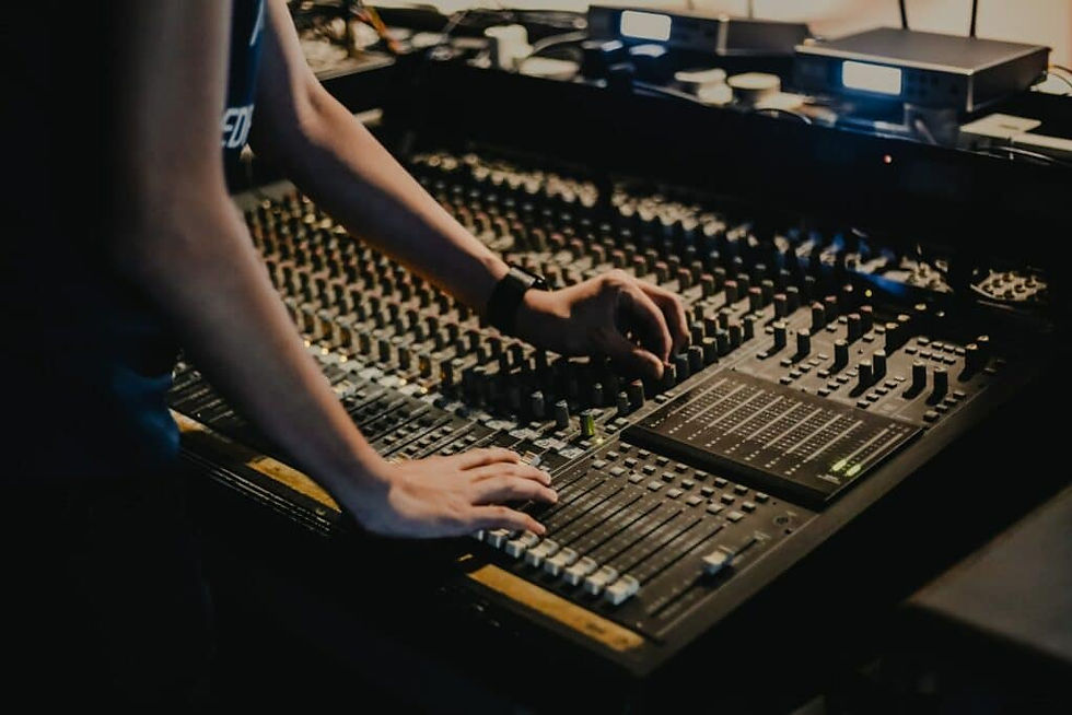 Personne ajustant les commandes sur une console de mixage audio en studio. Lumières tamisées, ambiance concentrée et professionnelle.