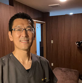 笑顔の男性、眼鏡をかけ、黒い服を着て立つ。内科医の市原です。