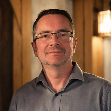 Board member in a grey button-down shirt and glasses.
