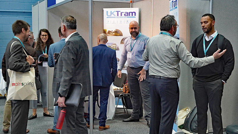 Delegates gather in a conference hall to network. The image shows the UKTram exhibitor and employees engaging with UK Light Rail Conference Members