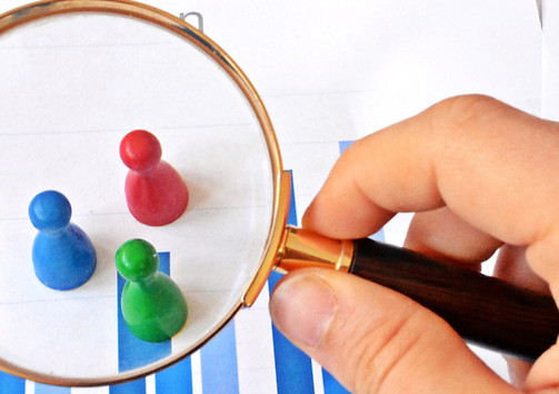 A young man is holding a magnifying glass in his hand, looking at statistic figures - a bu