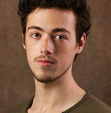 Joran - headshot of a male actor with curly hair, stubble, and wearing a green T-shirt, represented by ROC Talent Agency UK