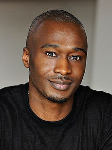 Michael - A headshot of a real model with a shaved head, light stubble, and a serious expression, wearing a black shirt, represented by Roc Talent Agency UK