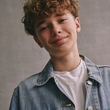 Toby - a headshot of a junior model with short curly hair, a natural smile, and wearing a white t-shirt and a denim shirt over the top, represented by ROC Talent Agency UK