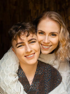 Beky and Rosie - headshot of a couple featuring a woman with shoulder length curly hair, a wide smile, with her arms wrapped around a woman with short curly hair and a wide smile, represented by ROC Talent Agency UK