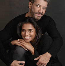 Anita and Bernado - headshot of a couple featuring a woman with long dark hair, a bright smile, sitting in front of a man with short hair and a natural expression, both wearing black, represented by ROC Talent Agency UK