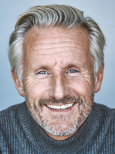 Simon - A headshot of a classic model with swept-back grey hair, light stubble, blue eyes, and a bright smile, represented by Roc Talent Agency UK