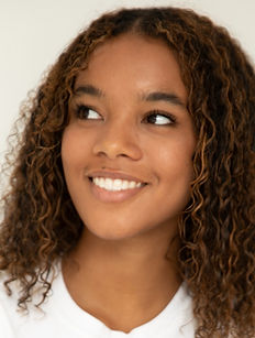 Leona - headshot of youth model with medium length curly hair, a bright smile and a wearing a white top, represented by ROC Talent Agency UK