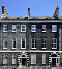 Two townhouses, designed with consistent, matching features. Black rendering with white stone framework.