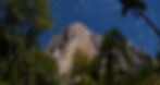 Star trails over a rocky mountain peak El Capitan surrounded by trees at night. The sky is clear and deep blue, creating a serene, majestic scene.