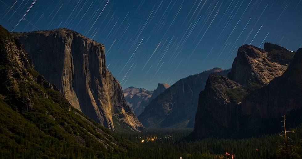 Yosemite Night sky with streaked star trails over a majestic mountainous landscape, illuminated by moonlight. Dark forests line the valley below.