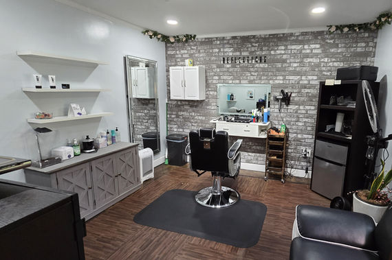 Salon interior featuring barber chair, mirror, storage, shelves, and brick wall with the sign WimbledonSalonSuites