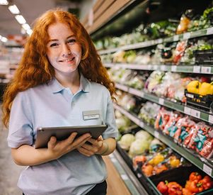 Closeup of a young worker with digital tablet in grocery store. Happy trainee working in s