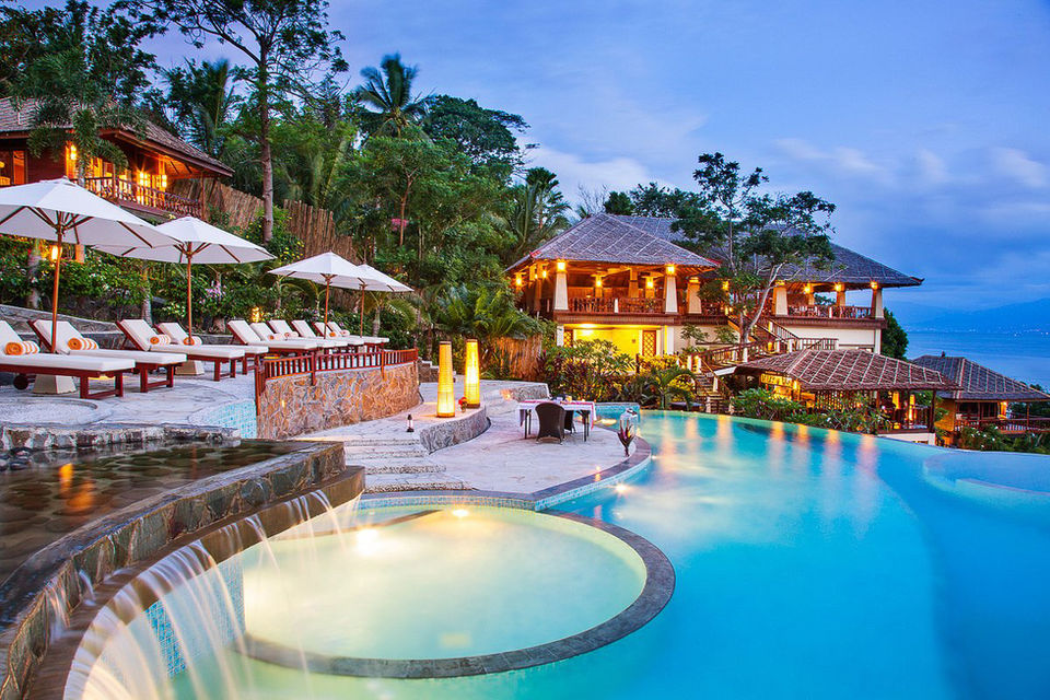 Luxury resort pool with umbrellas, lounge chairs, and ocean view at dusk.