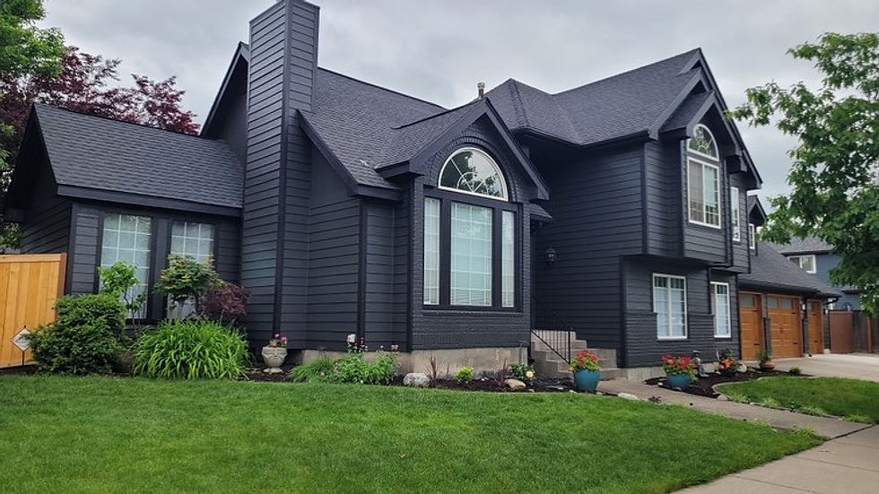 Dark gray house with large windows and a well-kept lawn. Overcast sky, trees, and shrubs enhance the tranquil suburban setting.