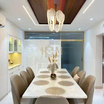 Contemporary dining area styled by hohm editors, interior designers in Hyderabad, featuring a custom marble dining table set with elegant grey upholstered chairs, open shelving with decorative crockery, sculpted vases, and warm accent lighting that highlights both the modern tableware and the sophisticated decor for elevated dining experiences.