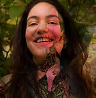 foto de Lina, mostrada do peito para cima. Ela tem pele clara, cabelos castanhos, compridos e ondulados. Sorri, olhando para frente. Sobreposta a foto, está o desenho de uma flor e uma folha.