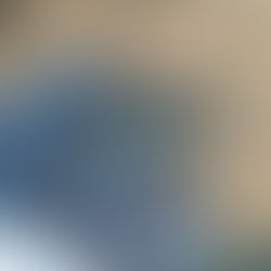 A paperback copy of House of Sky and Breath rests on top of a pair of legs which are wearing jeans. The background shows beige coloured patio stones.