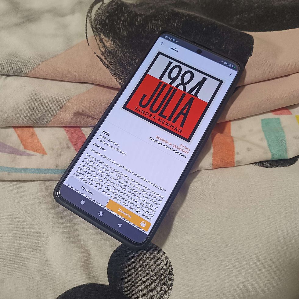 A phone rests on a blanket displaying the audiobook cover for Julia by Sandra Newman.