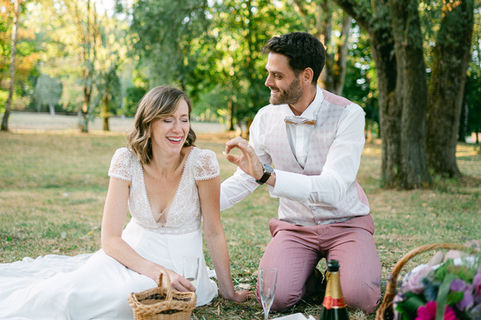 couple de mariés assis dans l'herbe qui rit pendant un pique nique