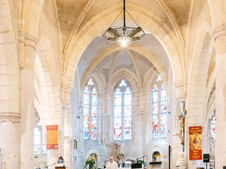 Mariage dans une église gothique, allée pleine d’invités, mariés devant l’autel, vitraux lumineux et bannières religieuses.