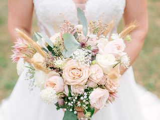 Mariée en robe blanche tenant un bouquet pastel de roses et fleurs séchées, en extérieur, ambiance douce.