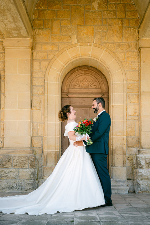 couple de mariés qui rigolent en se regardant. La mariée porte une longue robe blanche avec traîne et le marié un costume vert foncé