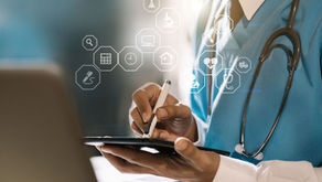 Médico com jaleco azul escrevendo em tablet com estetoscópio ao pescoço e ícones holográficos de saúde digital como coração, microscópio e hospital.