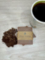 Jaxnrose Soaps Brewed Awakening Bar soap, brown soap surrounded by coffee beans. There is a cup of coffee sitting in the background. 