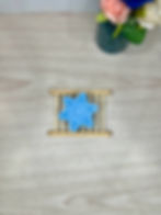Jaxnrose Soaps Bamboo Soap Dish with a blue snowflake bar of soap placed on it. There is a vase filled with roses and jacks in the background. 