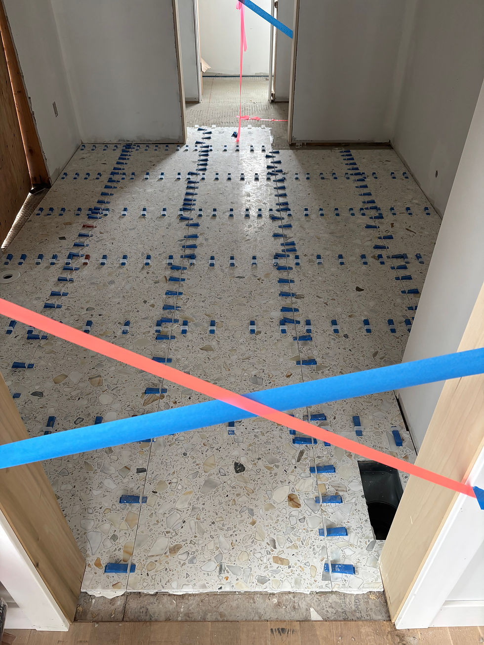Terrazzo floor installation in progress with blue spacers and red tape across doorway. White walls and a partially open door in the background.