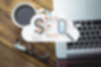 Cup of coffee, eyeglasses, and laptop on wooden table. SEO icons overlay with gears and magnifying glass, suggesting digital work theme.