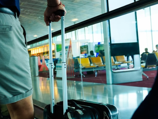 partial-back-view-of-person-pulling-luggage-through-airport-terminal