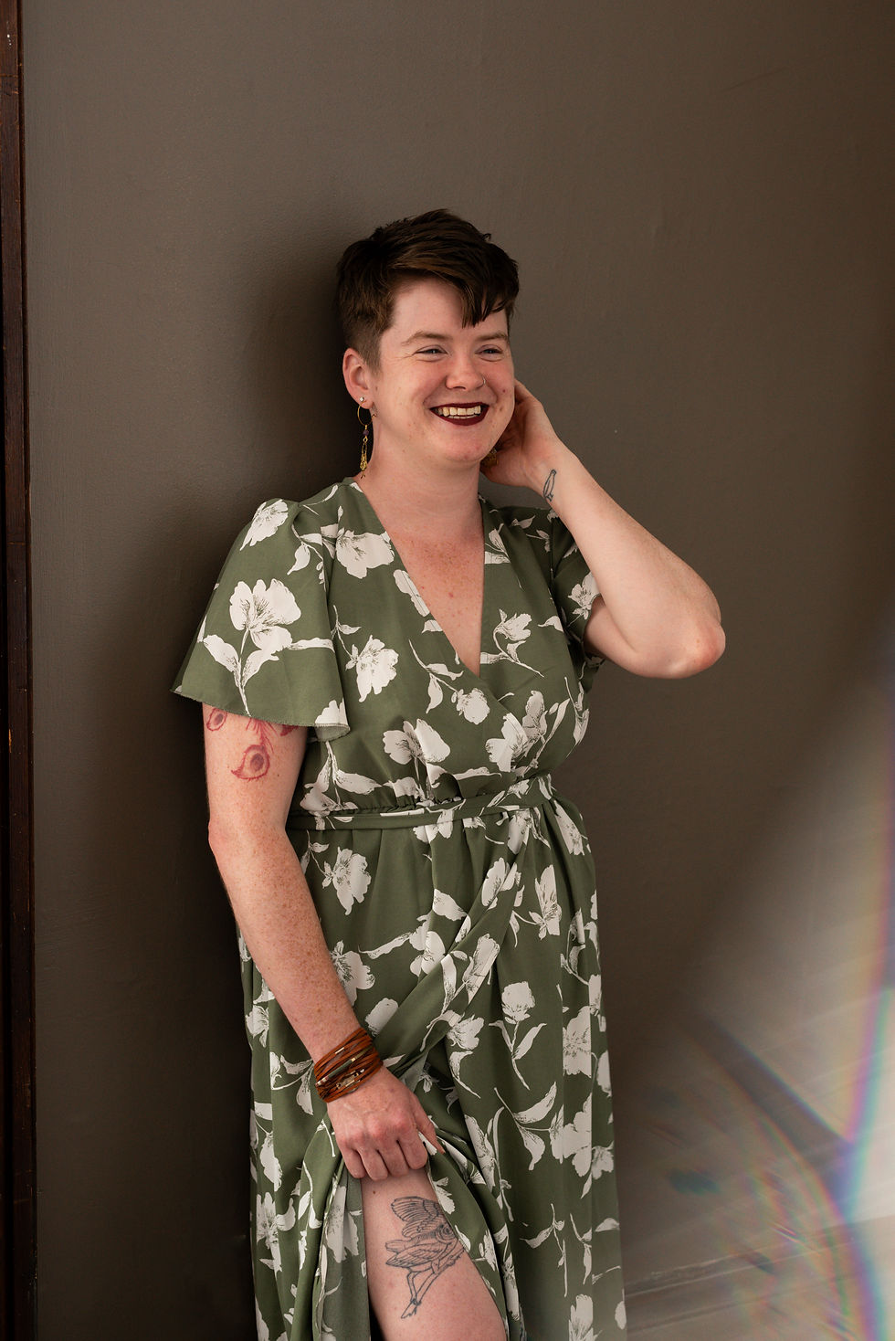 a picture of a brunette woman with short hair, smiling with eyes closed and looking away from the camera. She is wearing a green dress with white flowers