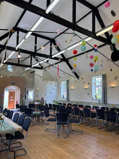 Tables and chairs set up inside hall with balloons and decorations.