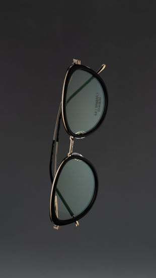 Minimalist product photograph of women’s cat-eye sunglasses floating against a soft dark gradient background. The frames feature refined craftsmanship and subtle color variations in titanium and acetate materials, highlighting modern eyewear design and elegant contours