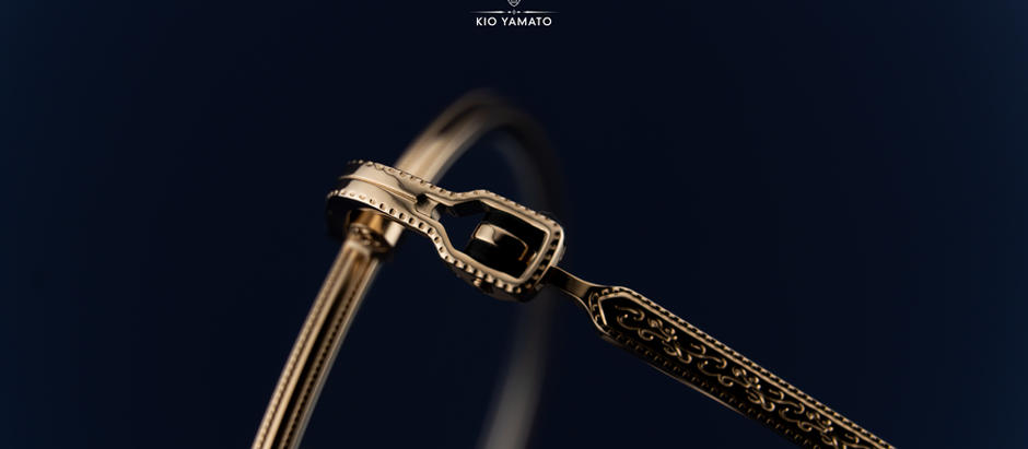 Close-up of a KIO YAMATO eyeglass hinge with dotted gold-tone edges and scrollwork engraved along the temple arm.