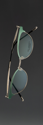 Minimalist product photograph of women’s cat-eye sunglasses floating against a soft dark gradient background. The frames feature refined craftsmanship and subtle color variations in titanium and acetate materials, highlighting modern eyewear design and elegant contours