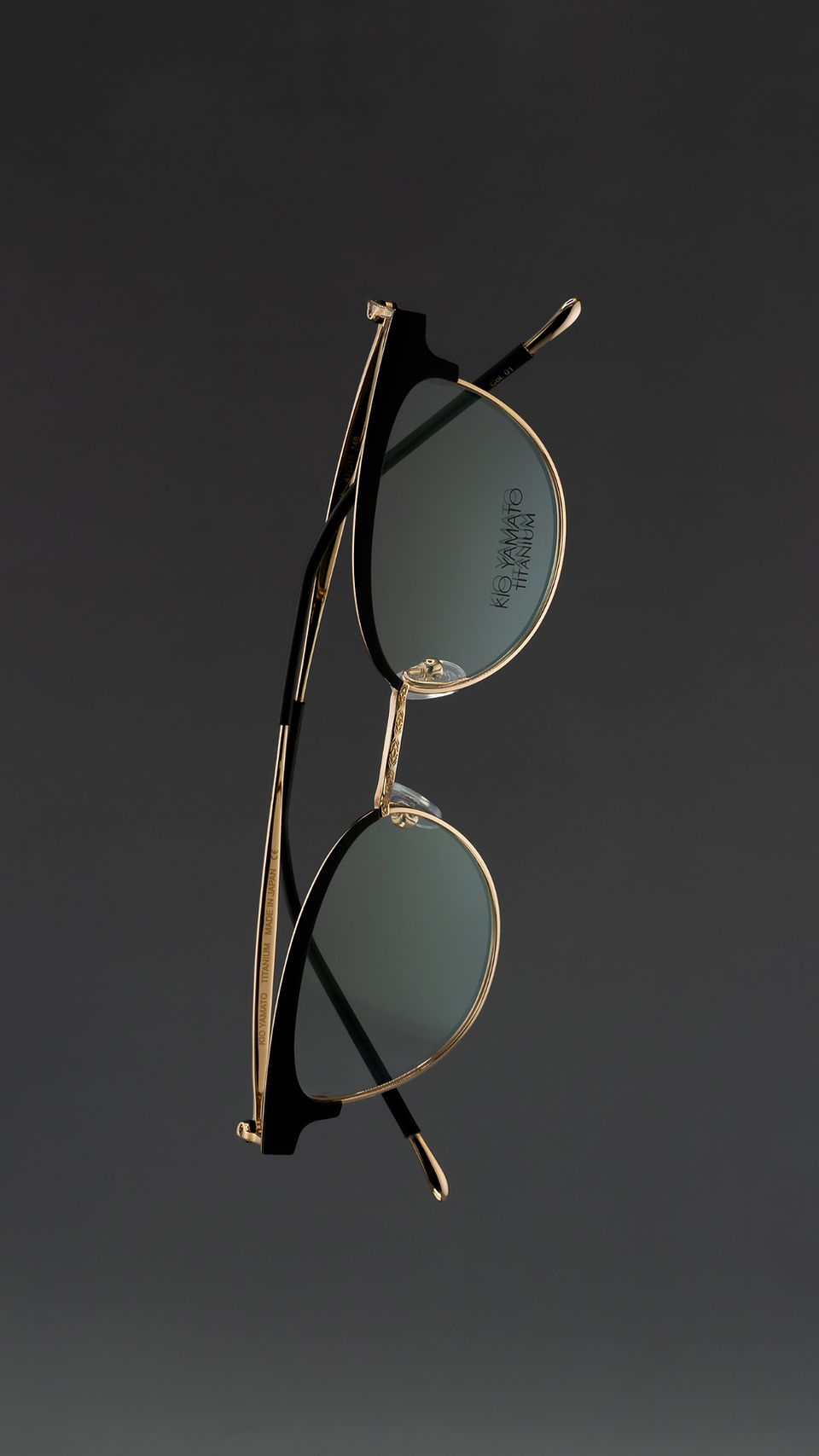 Minimalist product photograph of women’s cat-eye sunglasses floating against a soft dark gradient background. The frames feature refined craftsmanship and subtle color variations in titanium and acetate materials, highlighting modern eyewear design and elegant contours