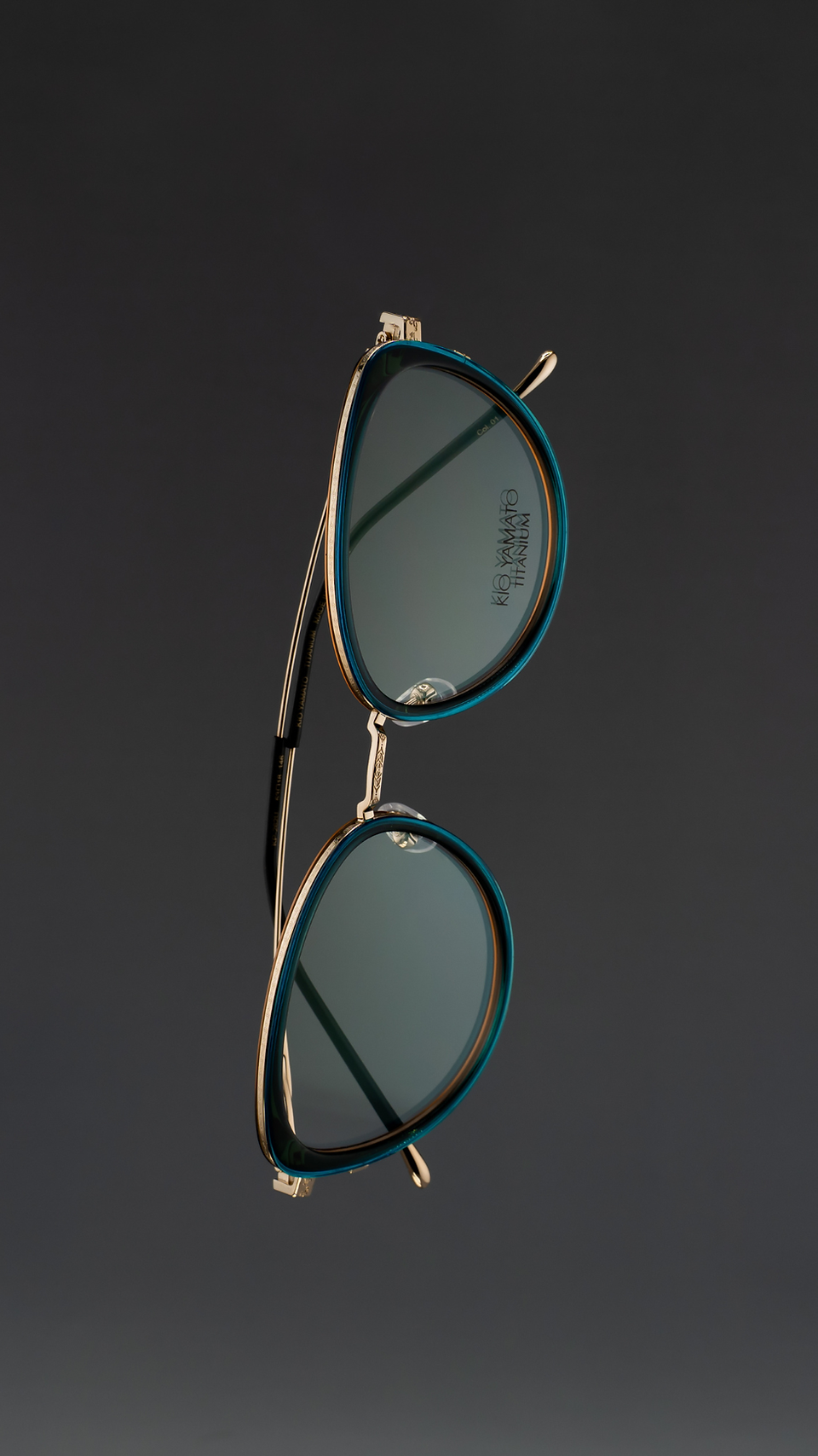 Minimalist product photograph of women’s cat-eye sunglasses floating against a soft dark gradient background. The frames feature refined craftsmanship and subtle color variations in titanium and acetate materials, highlighting modern eyewear design and elegant contours