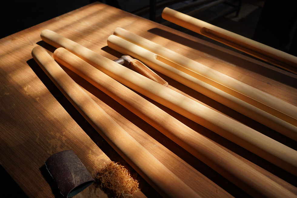 Smooth, hand-sanded custom wooden handrails resting on a craftsman's workbench bathed in warm sunlight, surrounded by a hand plane and fresh wood shavings at the THAVII studio.
