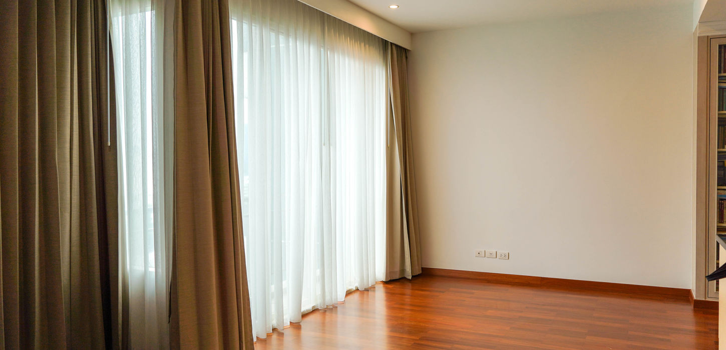 Modern high-end apartment living room in Bangkok featuring large glass windows with sheer and linen curtains, custom wood flooring, and integrated solutions by THAVII.