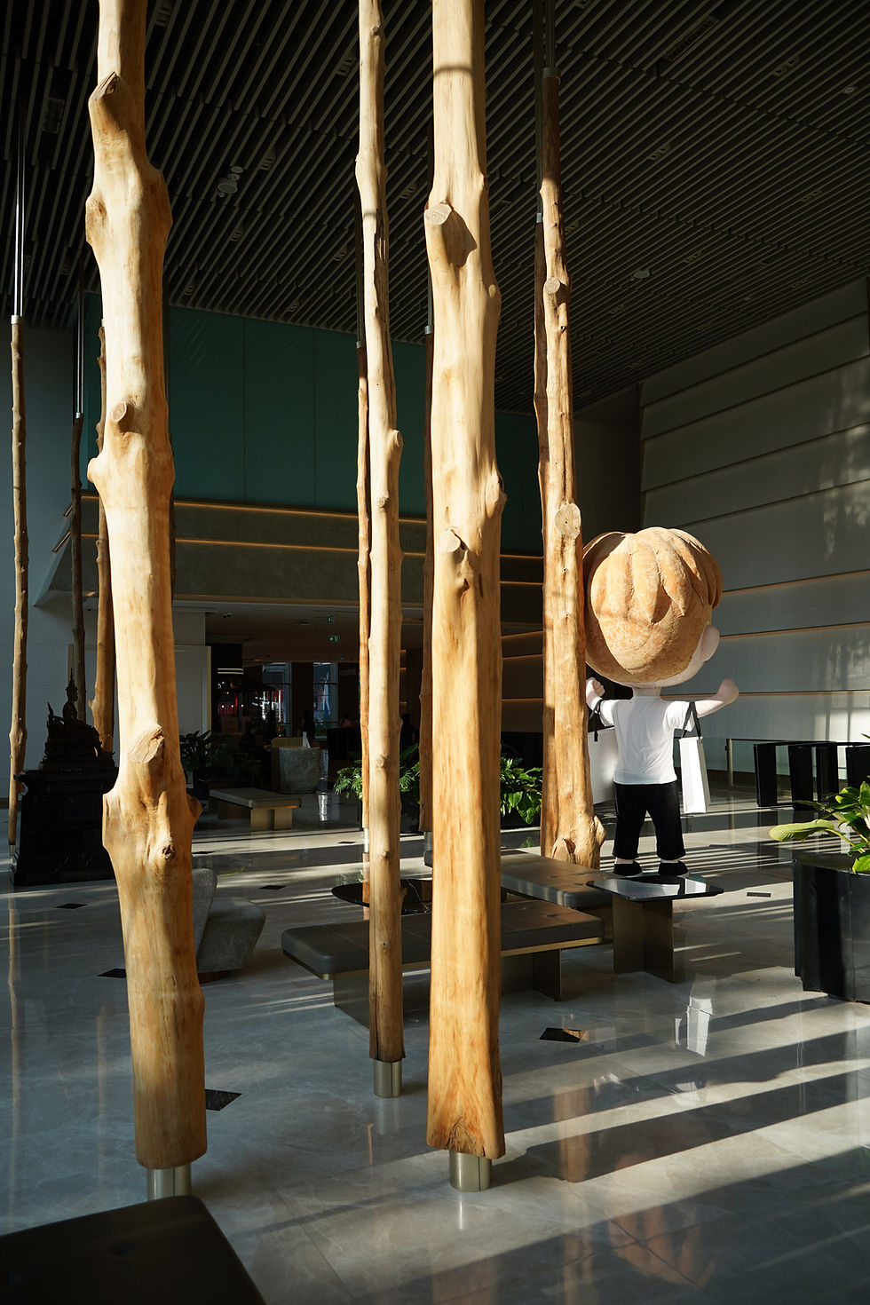 A grand, modern commercial lobby space showcasing massive, floor-to-ceiling organic raw wood pillars installed as architectural art, representing a unique large-scale project named "Park Silom Bangkok" collaboration by THAVII